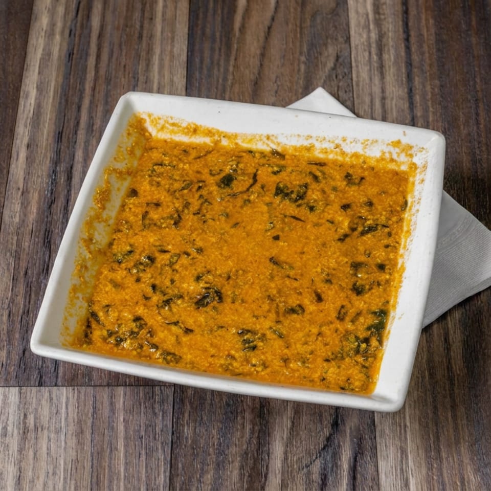 Square white dish filled with creamy orange curry speckled with herbs on a dark wooden table.